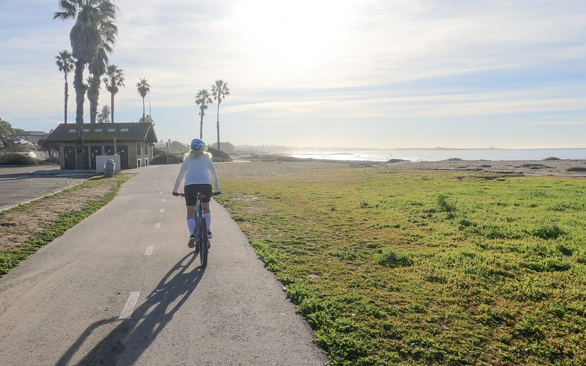 Female mountain biker follows pedestrian pathway along ocean